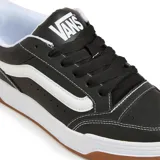 Championes Vans modelo Hylane, de diseño urbano con capellada de cuero sintético negro, franja lateral característica en blanco, suela de goma blanca y base de caucho color caramelo.