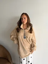 Buzo de textura tipo corderito en color beige, con cuello alto y cierre frontal parcial con tirador metálico decorativo. Presenta mangas largas con puños elásticos y un corte holgado.