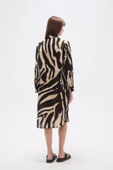 Vestido tipo camisa de corte holgado, con estampado de hojas en tonos marrones y beige. Presenta cuello camisero, cierre frontal con botones y mangas largas.