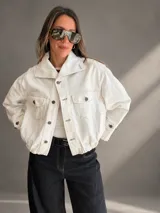 Campera bomber de denim blanco, confeccionada en mezcla de algodón y poliéster, con silueta relajada y largo a la cintura. Cuenta con cuello amplio, bolsillos delanteros con solapa, cierre frontal con botones y cintura elastizada.