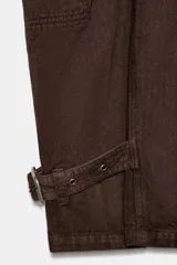Pantalón cargo de tiro medio confeccionado en algodón, con diseño de pierna ancha y costuras verticales. Presenta bolsillos laterales y bolsillos de plastrón con solapa en las piernas. El bajo es ajustable mediante trabillas y hebillas metálicas.
