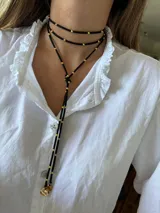 Gargantilla negra de cordón con detalle de pelotitas doradas y dijes circulares dorados en los extremos.