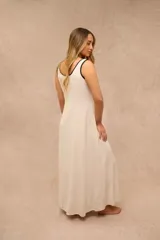 Vestido largo color crudo, sin mangas, con escote redondo y finos ribetes negros en el cuello y las sisas.