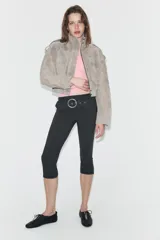Pantalón capri de tiro medio confeccionado en tejido elástico, con cintura elástica y detalle de cinturón integrado con hebilla metálica circular. Presenta aberturas en el bajo.