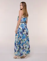 Vestido maxi largo de gasa estampada con diseño floral en tonos azules y verdes sobre base clara, de escote halter y sin mangas. Cuenta con cintura elastizada, lazo de ajuste y falda estructurada en paneles escalonados con forro interno.