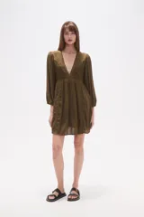 Vestido corto de color verde militar, con escote en V profundo, mangas largas con puños elásticos y detalles de encaje y bordados en el frente. Presenta una falda con vuelo y textura de pequeños puntos en relieve.