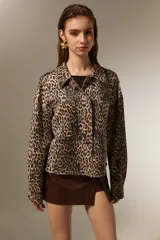 Chaqueta de corte recto con estampado animal print de leopardo, cuello camisero, cierre frontal con botones metálicos y bolsillos frontales tipo parche.