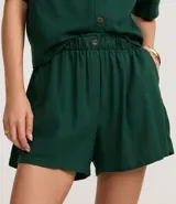 Short runner de viscolino, con cintura elástica, botón decorativo y bolsillos laterales. Presenta un corte evasé holgado con bajo redondeado.