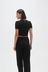 Top de manga corta con textura arrugada, cuello redondo y detalle de frunce frontal con argolla metálica y botón decorativo.