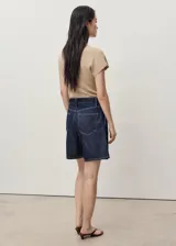 Short de jean azul oscuro con diseño recto, tiro medio y detalle de pinzas delanteras. Cuenta con cierre de cremallera y botón, trabillas para cinturón, dos bolsillos laterales y dos bolsillos traseros.