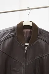 Campera tipo bomber de cuero ovino color marrón oscuro, con cuello de tejido acanalado y cierre frontal con cremallera.