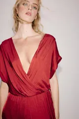 Mono largo satinado de color rojo, con escote en V cruzado y manga corta. Presenta cintura elástica con cinturón negro incorporado, bolsillos laterales ocultos y terminación de las piernas con puño elástico.