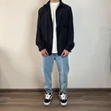 Sobrecamisa de pana negra con cuello clásico, cierre abotonado, manga larga con puños abotonados, bolsillo de parche en el pecho y corte recto. 