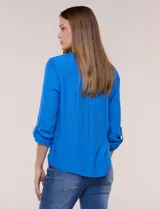Blusa de calce relajado color salmón, confeccionada en tela liviana con textura sutil. Presenta escote en V con abotonadura frontal, bolsillo parche en el pecho, mangas largas regulables con presilla y ruedo con opción de anudar en el frente.