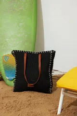 Bolso playero tipo canasto oversize tejido en papiro negro, con costuras decorativas en hilo blanco contrastante y asas de cuero marrón.