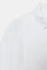 Camisa de algodón con cuello solapa y mangas por debajo del codo. Presenta un diseño con pechera plisada frontal, bajo recto y cierre mediante botones ocultos bajo solapa.