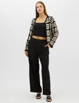 Cardigan abierto de tejido de punto calado con diseño geométrico bicolor en mangas y paneles frontales, y espalda en tono sólido. Presenta silueta recta, frente abierto sin cierre y terminaciones con vivos reforzados en escote, puños y ruedo.