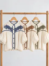 Blusa de algodón color off white con cuello mao, canesú con detalles de broderie y bordados, mangas cortas abullonadas tipo globo y cierre frontal con botones.