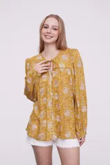 Blusa marrón con estampado de flores color naranja y blanco, con cuello redondo con abertura y mangas largas abullonadas.