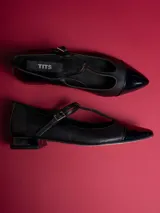 Chatitas negras de cuero sintético con punta charol y tira con hebilla.