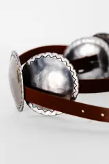 Cinturón marrón de cuero con apliques metálicos plateados de forma ovalada con borde irregular.