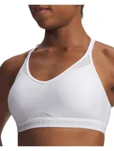 Top deportivo Under Armour de bajo impacto, color blanco, con diseño de espalda cruzada, paneles de malla para mayor transpirabilidad y banda elástica inferior con logo de la marca.