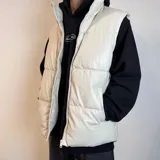 Chaleco puffer de cuero sintético en color negro, con diseño acolchado de paneles horizontales, cierre frontal completo y cuello alto.