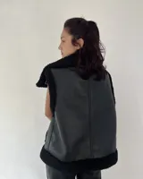 Chaleco estilo gamulán de cuero sintético marrón con interior y bordes de corderito sintético color crema. Presenta cierre frontal con botones a presión y bolsillos laterales.