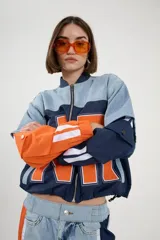 Campera corta estilo sporty chic con cierre frontal, confeccionada en denim celeste y tejido técnico azul y naranja. Presenta diseño color-block y corte holgado.