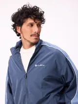 Campera rompevientos Rusty de nylon, color azul con detalles en azul claro en las mangas. Presenta cierre frontal, cuello alto y puños elásticos.