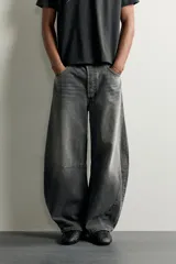 Jeans de denim de algodón color gris con efecto lavado, de corte relaxed barrel fit y tiro medio. Presenta diseño amplio con pinzas en las rodillas y costuras curvas, cierre frontal con botones y cinco bolsillos tradicionales.