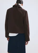 Chaqueta de algodón estilo tejano de corte recto, color marrón, con cuello camisero de efecto piel en contraste, manga larga y dos bolsillos de parche con solapa y botón en el frente. Cuenta con cierre oculto de cremallera y botones.