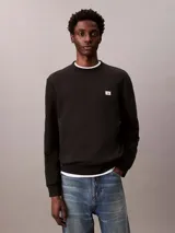 Buzo de algodón negro Calvin Klein, de cuello redondo, mangas largas y calce clásico. Presenta un pequeño parche con el monograma de la marca en el pecho y puños con ribete acanalado.