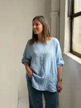 Blusa celeste de corte holgado, con cuello redondo, mangas tres cuartos con trabilla y detalles de alforzas en el frente.