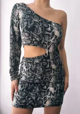Vestido corto con estampado de reptil en tonos grises y negros. Diseño asimétrico con un hombro descubierto y una manga larga. Presenta un corte en la cintura con detalle de argolla metálica.