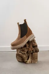 Botas tipo Chelsea con paneles elásticos laterales, confeccionadas en una combinación de cuero liso y gamuza en tonos marrones. Presentan una suela track robusta y dentada en color beige.