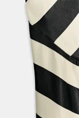 Vestido midi de satén con diseño a rayas diagonales en color negro y blanco crudo, escote halter con tirantes finos para anudar al cuello y espalda descubierta.