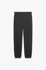 Pantalón negro de tiro medio con pinzas frontales, bolsillos laterales y falsos bolsillos de vivo en la espalda. El bajo termina en puño elástico.