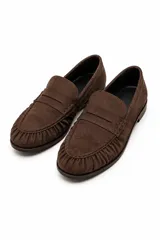 Mocasines de cuero negro con diseño clásico, punta redondeada con costuras fruncidas y tira decorativa en el empeine.