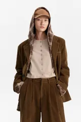 Blazer de pana marrón con solapas clásicas y botones oscuros. El forro de las mangas y la capucha superpuesta son de tela a cuadros en tonos marrones y beige.