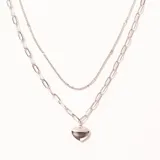 Colgante doble de acero plateado. Una cadena es fina y la otra de eslabones más grandes, con un dije de corazón liso y brillante.