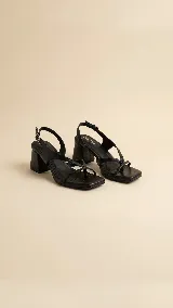 Sandalias de cuero negro con tiras cruzadas en el empeine y cierre de hebilla en el tobillo. Presentan un diseño de punta cuadrada y taco bloque de altura media.