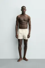 Short de baño de color beige con textura seersucker, cintura elástica con cordón ajustable, bolsillos laterales y forro interior.