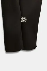 Pantalón de tiro alto con corte recto, cierre frontal con cremallera y botones decorativos en el bajo.