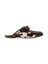 Zuecos Arno destalonados confeccionados en cuero con pelo con estampado animal print tipo vaca en tonos marrones, negros y blancos. Presentan diseño de inspiración náutica con cordones de cuero cruzados y ojalillos metálicos dorados.