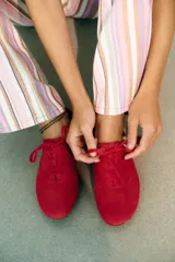Zapatilla deportiva estilo blucher de piel color rojo, con pespuntes en el cuerpo, cierre mediante cordones y punta redonda.