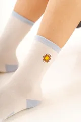 Medias de algodón color crema con detalles en celeste en el puño y talón, presentando un pequeño bordado de sol en el lateral.