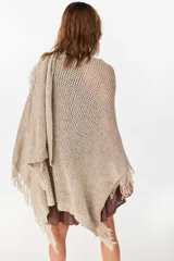 Ruana de punto color beige con diseño abierto y flecos en los bordes.