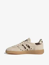 Championes Adidas Handball Spezial de diseño clásico, confeccionados en gamuza color crema con detalles de estampado animal print en las icónicas tres tiras y el talón. Presentan suela de goma color caramelo y logo dorado en el lateral.