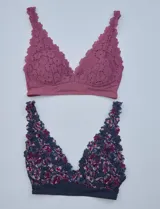 Pack de dos bralettes de encaje marca Jessica Simpson, con breteles fijos y espalda deportiva. Uno es de encaje floral color lila y el otro es de encaje floral multicolor sobre base azul.